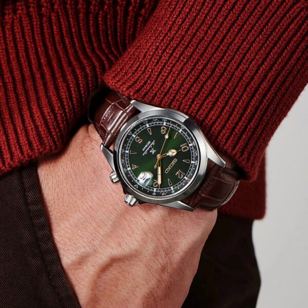 Close-up of a wristwatch with a green dial on a person's wrist wearing a red sweater.
