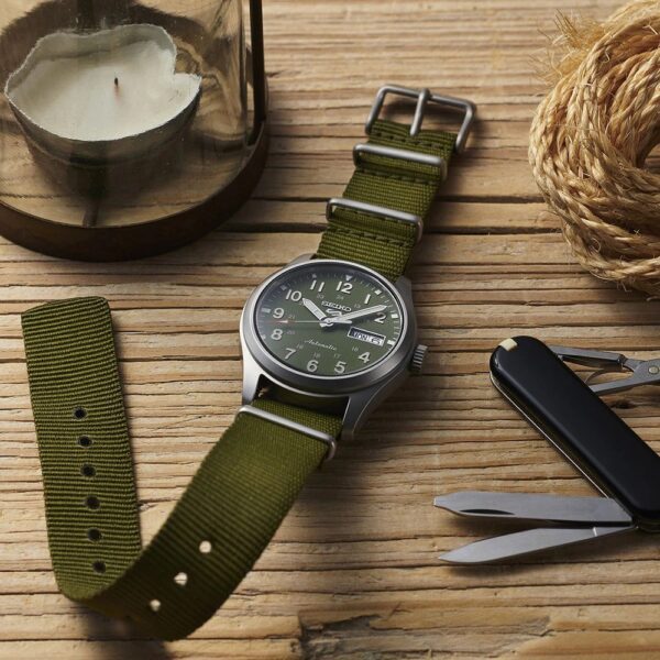 A green fabric strap wristwatch on a wooden surface with vintage tools.