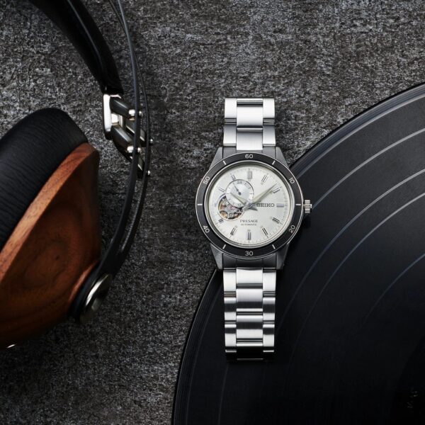 Silver wristwatch with a white dial beside headphones and a vinyl record.