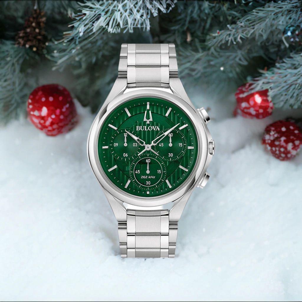 Silver wristwatch with green dial on snow with red berries.